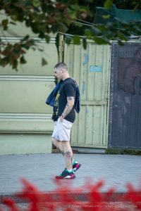 Фотография мужчины с татуировками на предплечье и голени, идущего по улице. Рисунок татуировки выполнен в темных тонах, с акцентом на графические элементы.