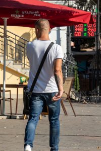 Фотография мужчины с татуировкой на плече, идущего по улице. Современный городской стиль, уверенный взгляд.