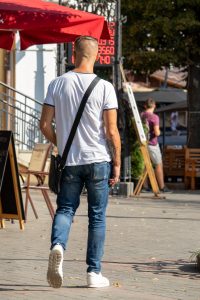 Фотография мужчины с татуировкой на плече, идущего по улице в белой футболке и джинсах. Современный городской стиль.