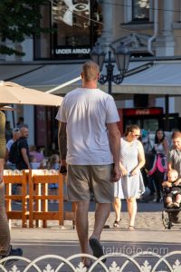 Фотография мужчины, идущего по улице, с заметной татуировкой в стиле трайбл на руке, выполненной в черных тонах.
