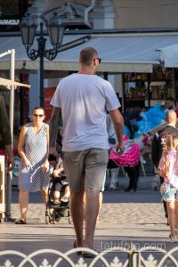 Фотография мужчины, идущего по улице, с заметной татуировкой в стиле трайбл на руке, выполненной в черных тонах.