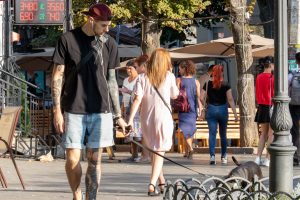 Фотография мужчины с татуировкой на плече и предплечье, идущего по улице. Тату выполнено в темных тонах, изображает абстрактные узоры и символы.