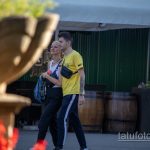 Фотография пары, идущей по улице, с акцентом на татуировку на руке мужчины и яркий фон уличной торговли.