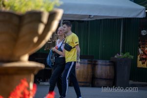 Фотография пары, идущей по улице, с акцентом на татуировку на руке мужчины и яркий фон уличной торговли.