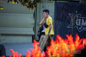 Фото молодого человека с татуировкой на руке, изображающей букет пионов в серой гамме. Современный стиль, городской пейзаж.