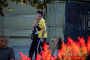 Фото молодого человека с татуировкой на руке, изображающей букет пионов в серой гамме. Современный стиль, городской пейзаж.
