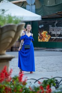 Фото тату на плече девушки в синем платье. Небольшая татуировка, выполненная тонкими линиями, добавляет образу изысканности.