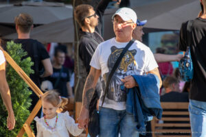 Фото тату тигра на руке мужчины в повседневной одежде, идущего по улице с ребенком. Реалистичный рисунок татуировки с детальной проработкой шерсти.