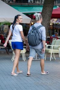 Фотография пары, идущей по улице, держась за руки. У девушки на шее видна татуировка, у мужчины - на руке.