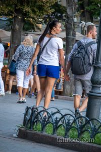 Фотография пары, идущей по улице, держась за руки. У девушки на шее видна татуировка, у мужчины - на руке.