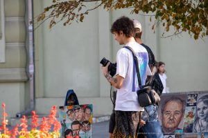 Фото тату: мужчина-фотограф с татуировками на руках, снимает на камеру. Видны небольшие рисунки татуировок на предплечье и кисти.