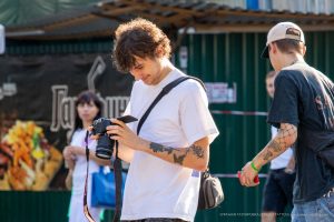 Фотография татуировки на предплечье: стилизованный черный ворон в полете с красными брызгами краски, выполненный в графическом стиле.