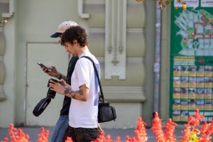 Фото тату: мужчина-фотограф с татуировками на руках и частично видимой татуировкой на спине, смотрит в смартфон.