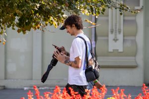 Фото тату: мужчина-фотограф с татуировками на руках, смотрит в смартфон. Видны небольшие рисунки татуировок на предплечье.