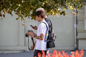 Фото тату: мужчина-фотограф с татуировками на руках, смотрит в смартфон. Видны небольшие рисунки татуировок на предплечье.