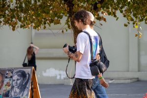 Фото тату: мужчина-фотограф с татуировками на руках, снимает на камеру. Видны небольшие рисунки татуировок на предплечье.