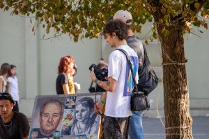Фото тату: мужчина-фотограф с татуировками на руках и частично видимой татуировкой на спине, снимает на камеру.