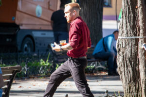 Фото тату на предплечье мужчины, держащего стакан с напитком на улице. Рисунок татуировки выполнен в темных тонах, с акцентом на детали.
