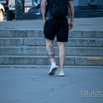 Фото тату корабля на икре мужчины, идущего по лестнице. Черно-серый рисунок татуировки в реалистичном стиле.