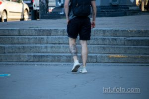 Фото тату корабля на икре мужчины, идущего по лестнице. Черно-серый рисунок татуировки в реалистичном стиле.