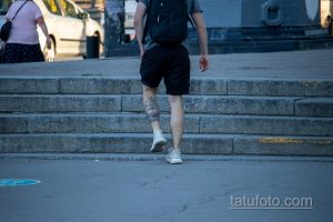 Фото тату корабля на икре мужчины, идущего по лестнице. Черно-серый рисунок татуировки в реалистичном стиле.