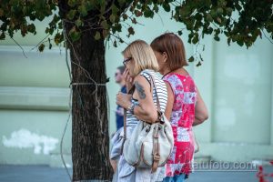 Фото тату на плече женщины в полосатой майке. Татуировка выполнена в темных тонах и частично видна под одеждой.