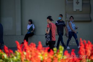 Фото тату на руке мужчины в кепке и футболке с принтом. Татуировка выполнена в черных тонах и видна на фоне ярких красных цветов.