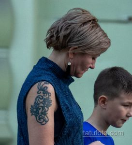 Фотография крупным планом татуировки на руке женщины: темный орнамент, расположенный на плече. Видна текстура кожи.