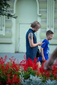 Фотография женщины с татуировкой на руке и ребенком рядом. Татуировка представляет собой темный орнамент, расположенный на плече.