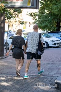 Фото тату на икре мужчины: абстрактный черно-серый рисунок, напоминающий узор из геометрических фигур и линий. Виден на фоне повседневной городской обстановки.