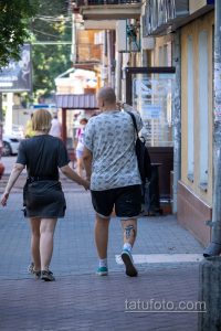 Фото мужчины с татуировкой на ноге, идущего по улице. Татуировка выполнена в темных тонах и видна из-под шорт.