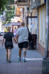 Фото мужчины с татуировкой на ноге, идущего по улице. Татуировка выполнена в темных тонах и видна из-под шорт.
