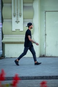 Фото тату: Мужчина в черной футболке и кепке с татуировками на руке, включая изображение черепа и надпись 'ALIEN'.