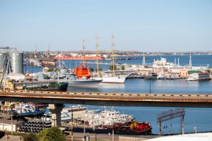Вид на Одесский порт с высоты. Корабли, парусники, мост и причалы создают живописную морскую панораму.