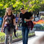 Фотография пары, прогуливающейся в парке. У мужчины на предплечье видна татуировка с детализированным рисунком.