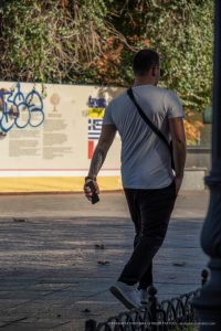 Фото тату: Мужчина в белой футболке с татуировкой на руке, держащий смартфон. Татуировка выполнена в темных тонах и имеет сложный узор.