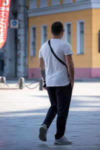 Фотография мужчины с татуировкой на предплечье, идущего по улице. Татуировка выполнена в стиле трайбл, черного цвета.