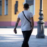 Фотография мужчины с татуировкой на предплечье, идущего по улице. Татуировка выполнена в стиле трайбл, черного цвета.