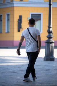 Фотография мужчины с татуировкой на предплечье, идущего по улице. Татуировка выполнена в стиле трайбл, черного цвета.
