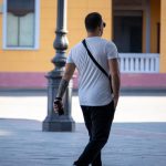 Фотография мужчины с татуировкой на предплечье, идущего по улице. Татуировка выполнена в стиле трайбл, черного цвета.