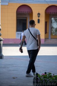 Фотография мужчины с татуировкой на предплечье, идущего по улице. Татуировка выполнена в стиле трайбл, черного цвета.