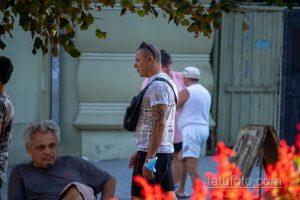 Фото тату на плече мужчины: темная полинезийская графика, покрывающая часть руки. Мужчина идет по улице, одетый в повседневную одежду.