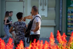 Фото татуировки на плече мужчины. Темный узор, напоминающий морской узел или якорь, на фоне газетных вырезок. Расположена на плече.