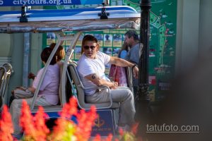 Фото татуировки на руке мужчины в туристическом автобусе. Темный узор, вероятно, геометрический или абстрактный, расположен на предплечье.