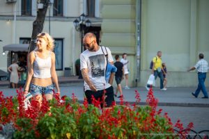Фотография пары, идущей по улице. У мужчины и женщины видны татуировки на руках. Летний день, городская среда.