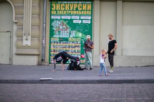 Фотография уличного акробата, выполняющего стойку на руках на фоне городской стены с афишами в Одессе. На руке видна татуировка.