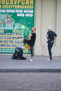 Фотография двух мужчин, стоящих на фоне городской стены с картой Одессы. Татуировки на руках, современный стиль и динамичная атмосфера.