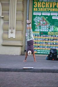 Фотография мужчины, выполняющего стойку на руках на фоне городской стены с картой Одессы. Татуировки на руках, спортивный стиль и динамичная поза.