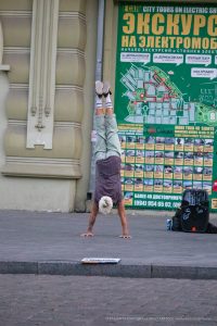 Фотография мужчины, выполняющего стойку на руках на фоне городской стены с картой Одессы. Татуировки на руках, спортивный стиль и динамичная поза.