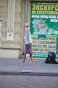 Фотография мужчины, выполняющего стойку на руках на фоне городской стены с картой Одессы. Татуировки на руках, спортивный стиль и динамичная поза.